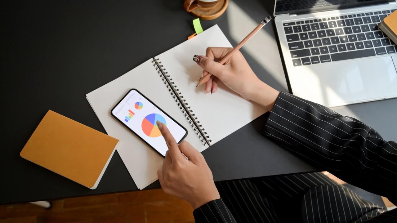 property management professional writing in a notebook and looking at a pie chart on their smart phone