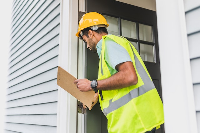 Person in a yellow hard hat and high visibility vest inspecting the exterior of a property