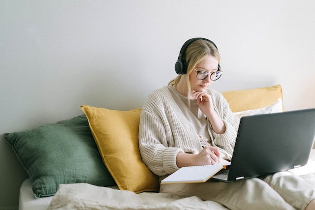 Person sitting on a couch wearing black headphones and researching Bay Area investment properties on their laptop